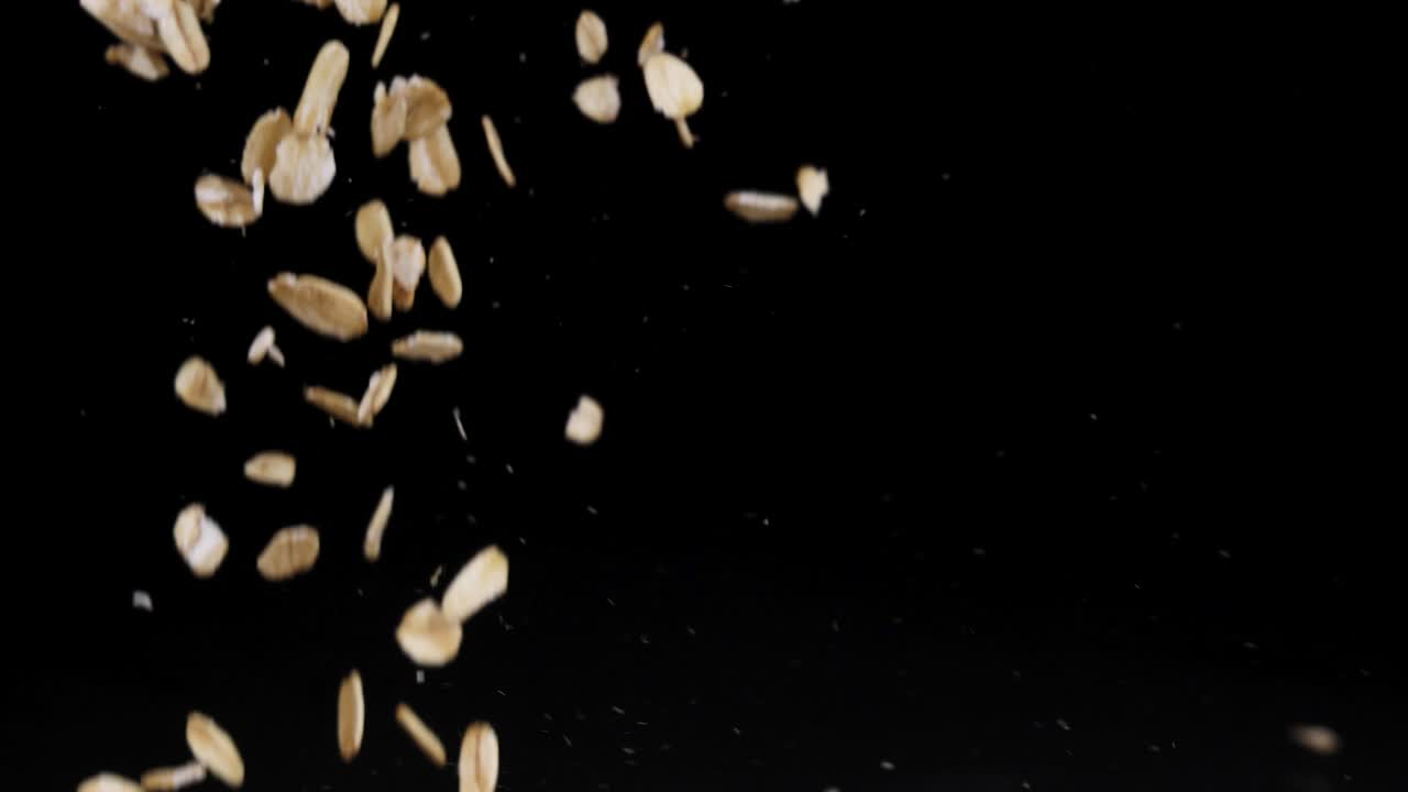 Oats cascade from a wooden spoon against a black background, captured in slow motion with dramatic lighting