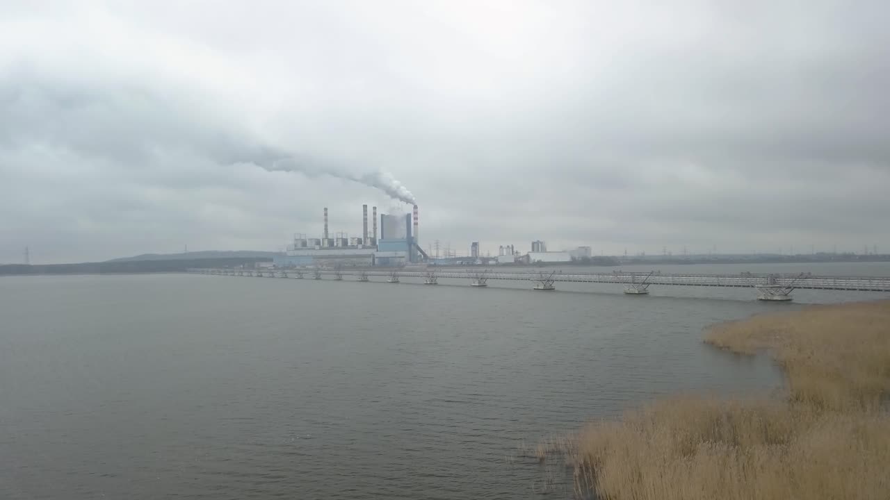 drone fly above river with power plant industry scenario landscape at distance under clouds dramatic sky