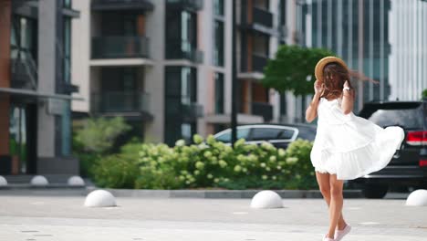 mujer con vestido blanco y sombrero de paja caminando por la ciudad