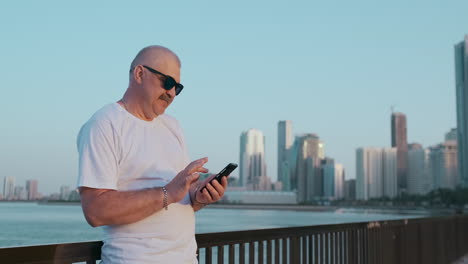 Low-angle-view-of-attractive-business-man-over-blurred-street-background-holding-smart-phone-in-hands-using-4G-internet-chatting-with-friends-searching-contact.-Electronic-wireless-device-concept.