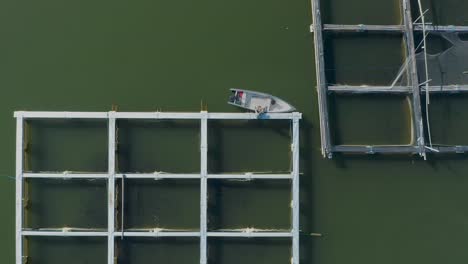 Lokaler-Fischer,-Der-Ein-Boot-Auf-Einem-Quadratischen-Schwimmenden-Fischfarmrahmen-Anlegt,-Von-Oben-Nach-Unten