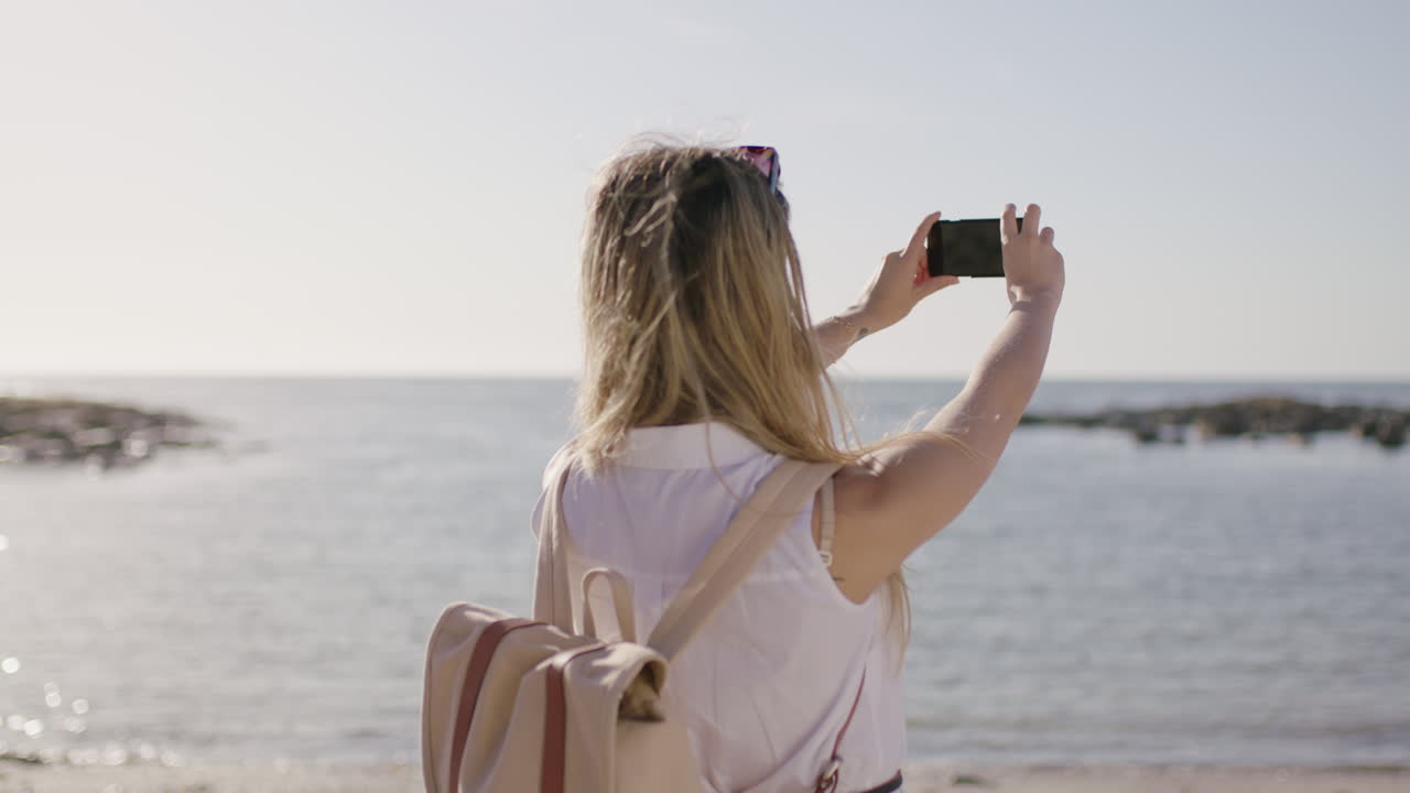 아름다운  ⁇ 은 해변에서 젊은 여성의 초상화 휴대폰을 사용하여 사진을 찍고
