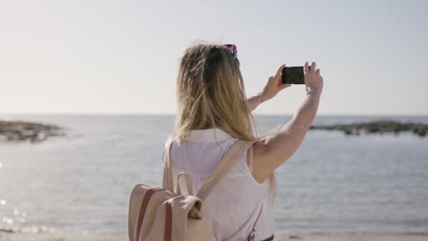Retrato-De-Una-Mujer-Joven-En-Una-Hermosa-Playa-Soleada-Tomando-Fotos-Usando-El-Teléfono