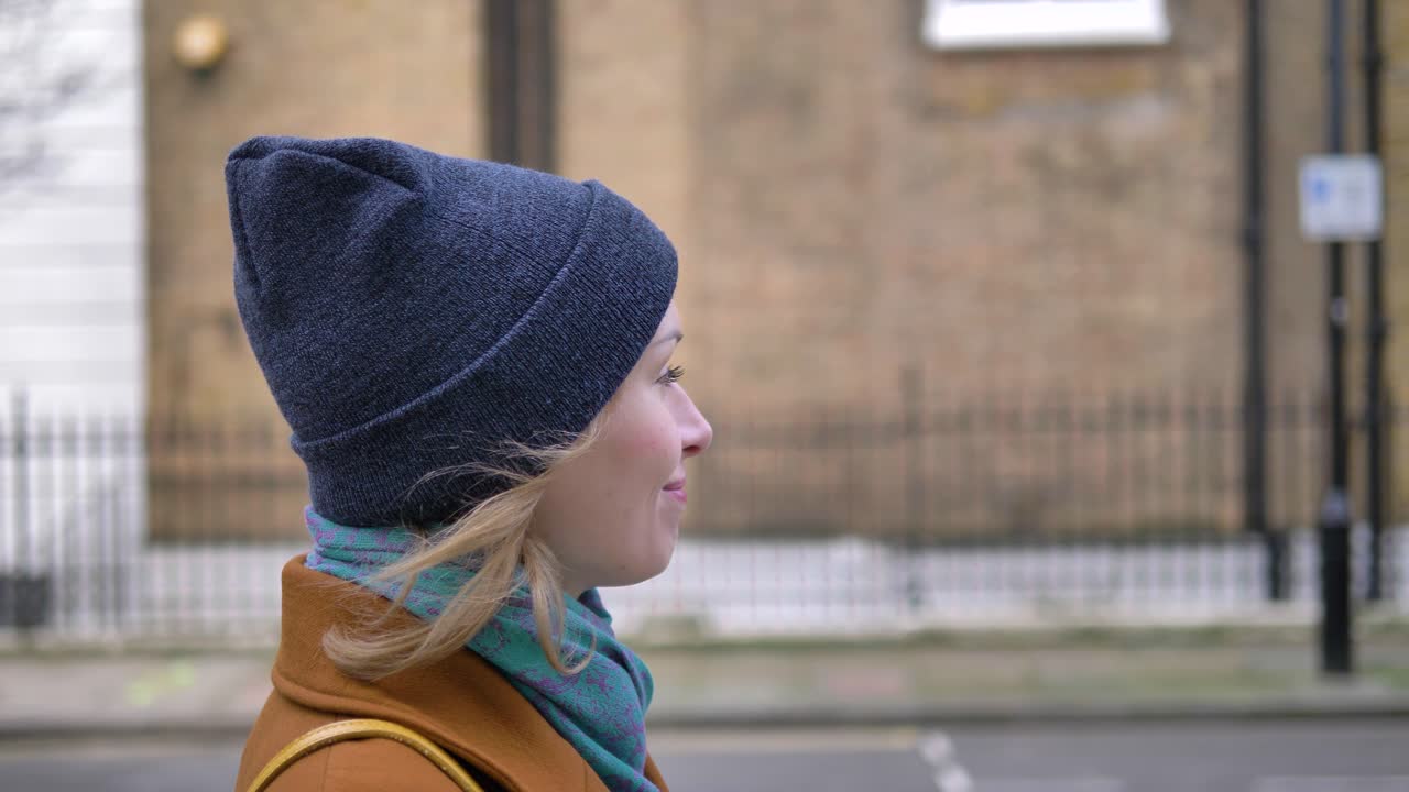 Side closeup view of a happy cheerful positive and relaxed young Caucasian woman enjoying the weather, walking down a London street and smiling while looking around
