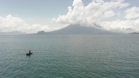 man on small boat on atitlan lake and surrounding landscape, guatemala