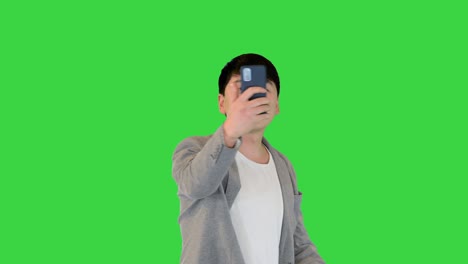 젊은 아시아 남자가 녹색 화면, 크로마 키에서 비디오 통화를 하고 고 있습니다.