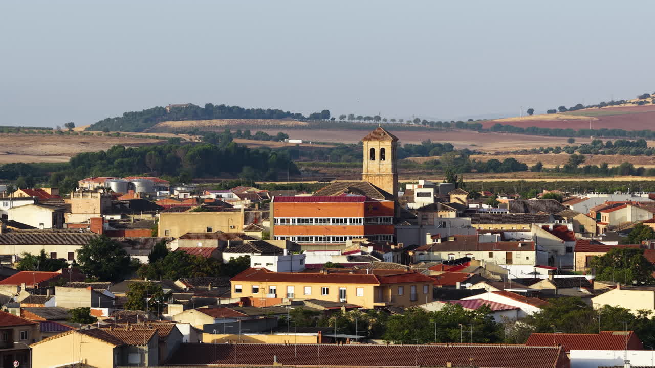 Veduta aerea con drone di una piccola città con case tradizionali e campanile, circondata da paesaggio agricolo nella campagna spagnola