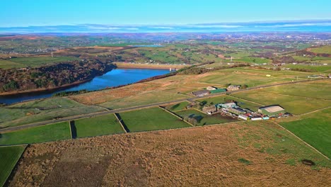 country road with the m62 motorway in the distance,crossing scammonden dam with farmland lake, reservoir, and wide open views of the pennine hills