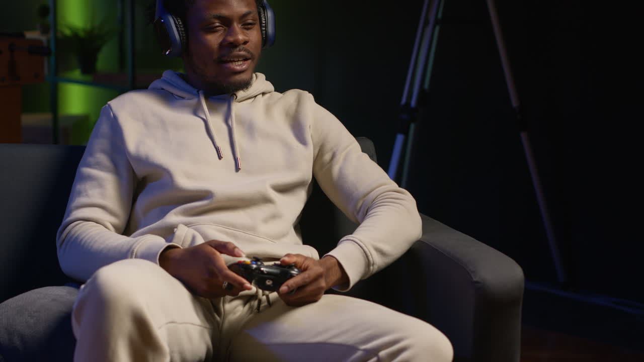 African american person in his cozy loft playing video games tournament, relaxing and having fun. Gamer in multiplayer game on gaming console during leisure time at home. Camera A.