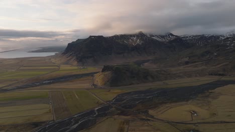 Luftpanorama-Der-Landschaft-Eines-Flusses,-Der-Aus-Einem-Gebirgstal-In-Island-Herabfließt,-Mit-Einer-Dramatischen-Wolkenlandschaft-Am-Abend