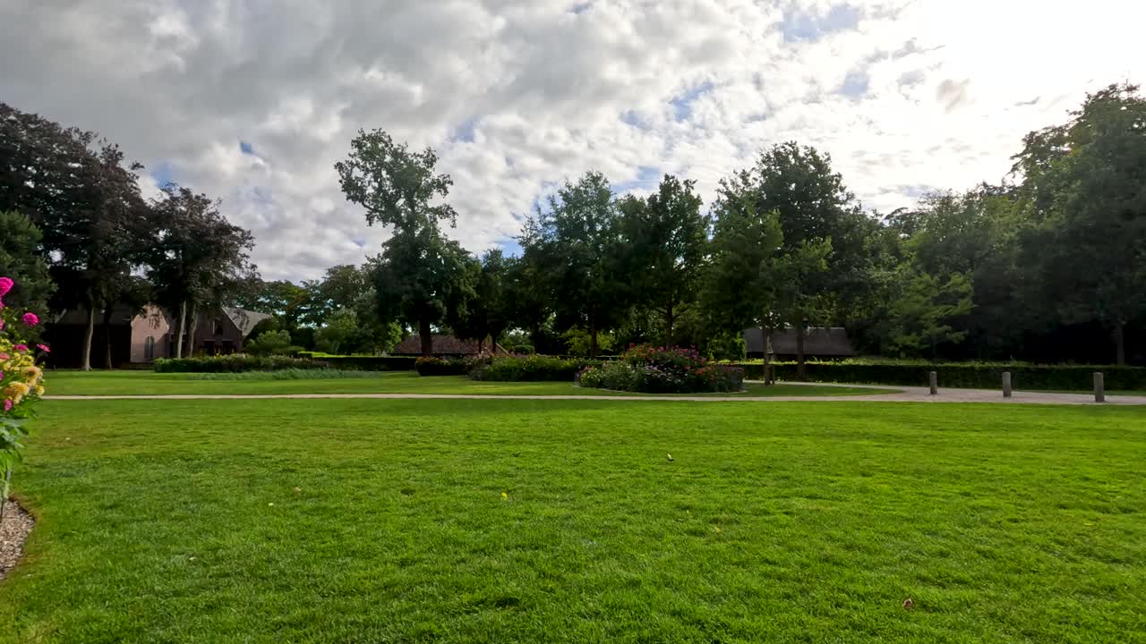 A smooth, wide-angle camera pan reveals vibrant flower beds, manicured lawns, and lush trees under dramatic cloudy daylight in a formal garden