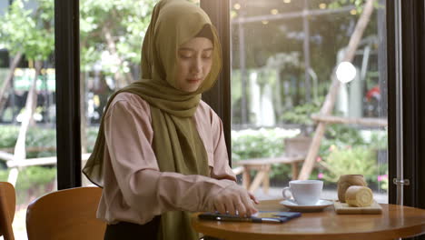 Una-Mujer-Musulmana-Asiática-Con-Movilidad-Ascendente-Que-Disfruta-De-Un-Momento-Relajante-En-La-Cafetería-En-Un-Día-Soleado