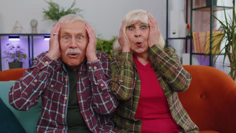 Wow,-excited-amazed-senior-old-man-woman-raising-hands-in-surprise-looking-at-camera-with-big-eyes