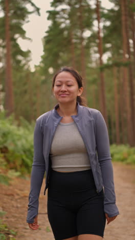 Vertical-Video-Of-Woman-Wearing-Sports-Clothing-Exercising-Looking-Around-Walking-Along-Track-In-Forest-Enjoying-Peace-And-Beauty-Of-Nature-Shot-In-Real-Time