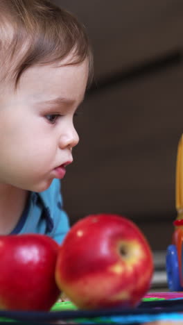 sweet lovely child lies on the floor with some apples in front of him. adorable toddler touching the bright toy car, opening and closing the car door. close up.
