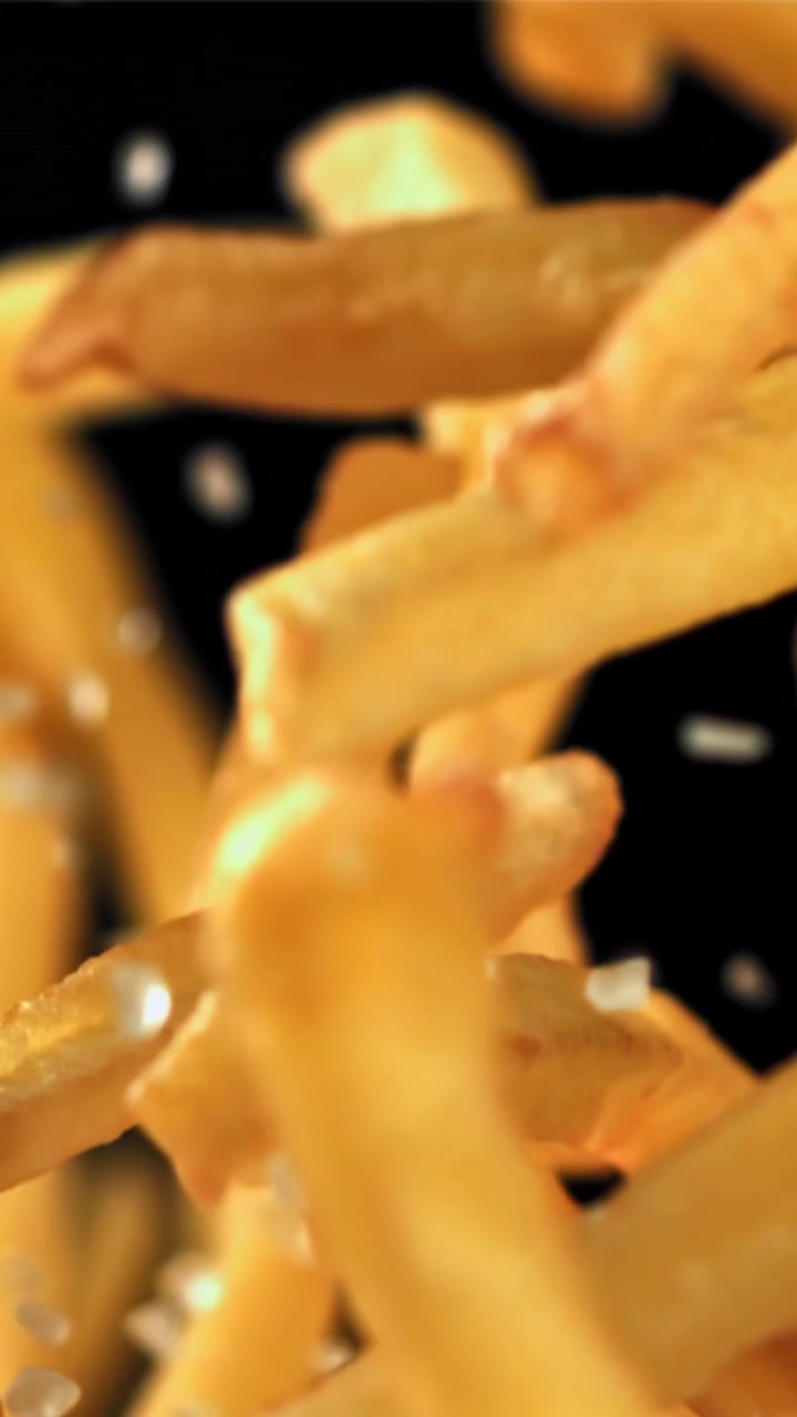 Patatine fritte dorate che cadono con il sale su sfondo nero.