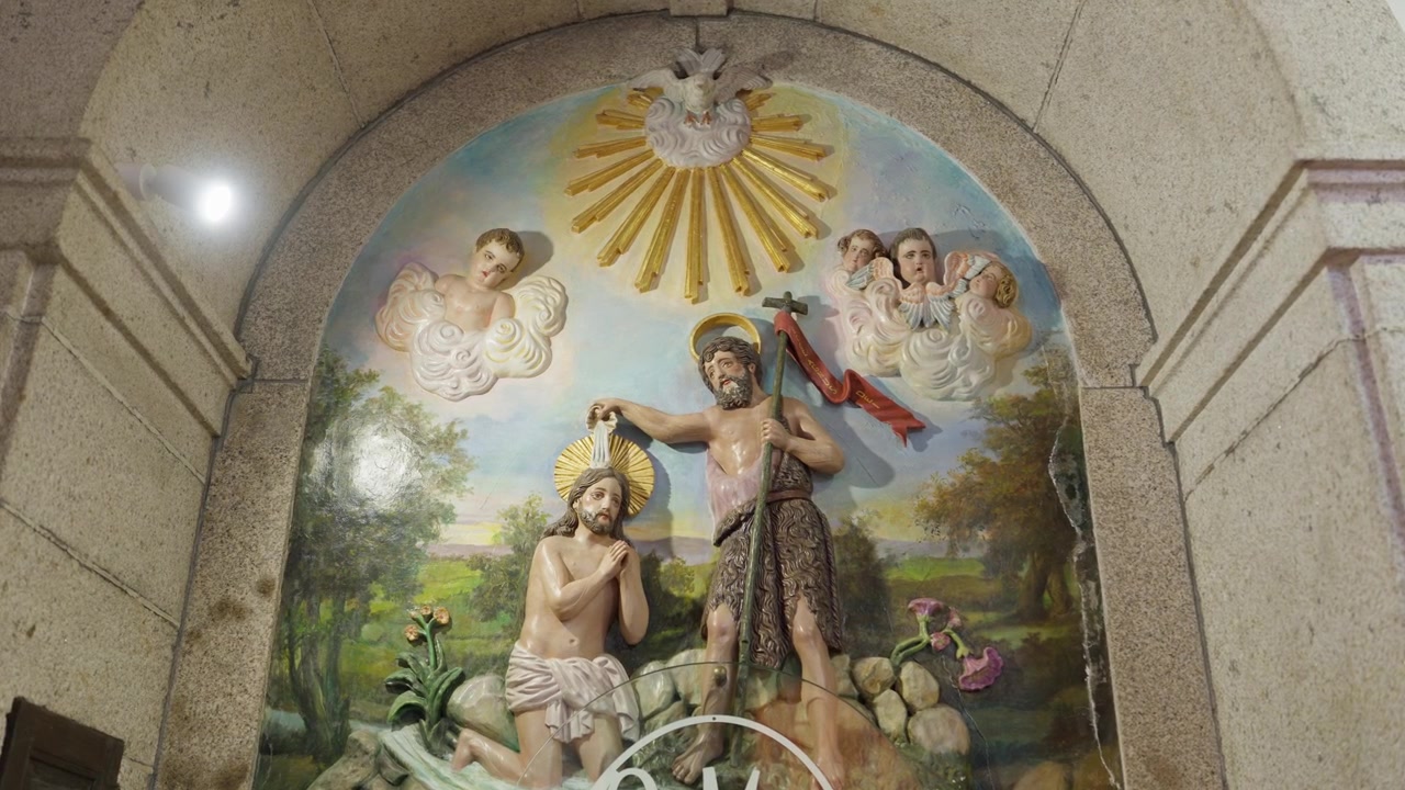 Rilievo dipinto del Battesimo di Cristo con angeli e colomba all'interno di una nicchia ad arco in pietra