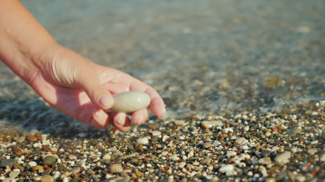 한 여자의 손이 서핑 4k 비디오의 배경에 조약돌을 들고 있다