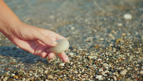 La-Mano-De-Una-Mujer-Sostiene-Una-Piedra-Contra-El-Fondo-Del-Video-De-Surf-4k