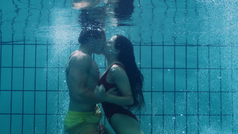 Pareja-Romántica-Besándose-Bajo-El-Agua-En-La-Piscina-Jóvenes-Enamorados-Disfrutando-De-Besos-íntimos-Amantes-Sumergidos-En-Agua-Flotando-Con-Burbujas-En-Intimidad-Apasionada