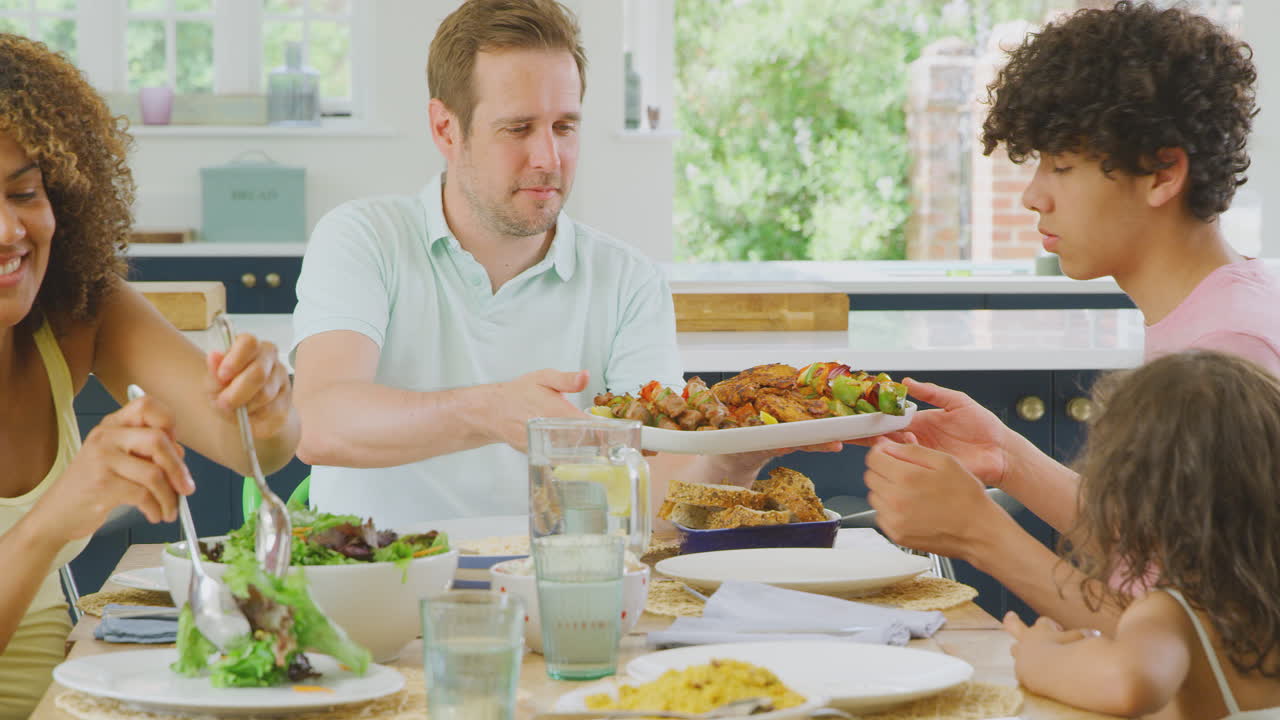 familia multirracial sentada alrededor de la mesa en la cocina en casa comiendo juntos
