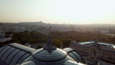 drone tour of paris city from above, with french flag waving on top of grand palais and petit palais at the dawn, highlighting silhouette view of sacre coeur at distance
