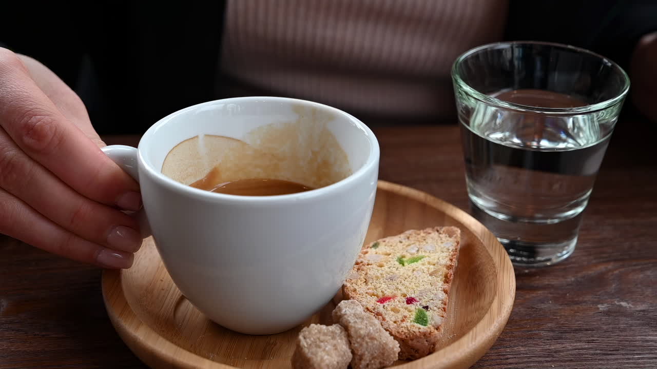 Close up of a woman drinking an espresso with biscotti near a glass of water at a cafe