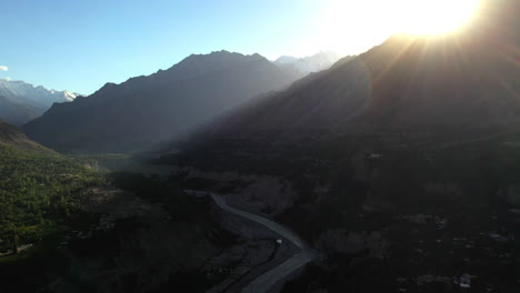 Epic-drone-shot-of-sun-rays-shining-in-the-valley,-Passu-Cones-in-Hunza-Pakistan,-snow-covered-mountain-peaks-with-steep-cliffs,-high-wide-aerial-shot