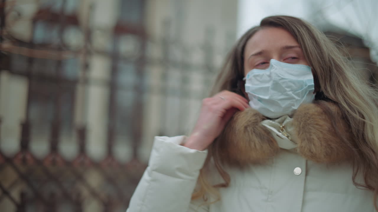 A woman in a white winter coat carefully gets off a medical mask outdoors on a cold day