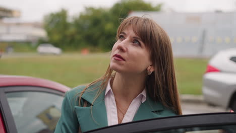 Focused-businesswoman-stands-near-car-looking-at-building