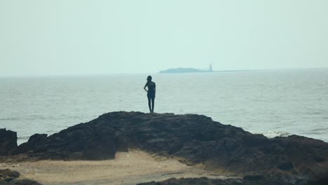 girl-standing-on-rock-moving-sea-waves-in-back-long-shot