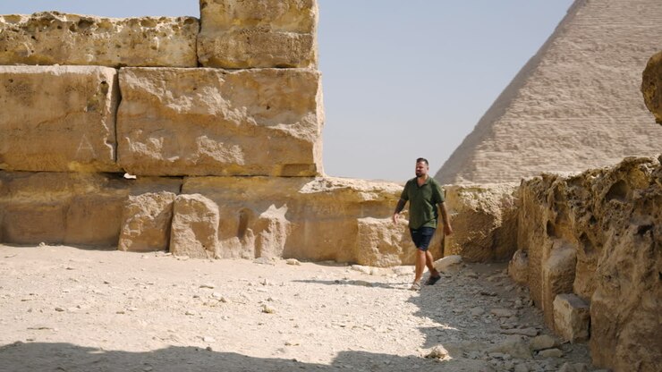 A Man Standing Near Limestone Blocks at the Giza Plateau, Admiring the View of the Pyramids, Near Cairo, Egypt - Tracking Shot