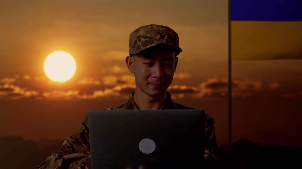 Soldato che lavora al portatile al tramonto con bandiera ucraina sullo sfondo