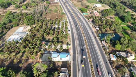 drone view of a busy highway in karnataka. it runs alongside extensive coconut trees, with vehicles traveling. ideal for themes of regional development and rural connectivity