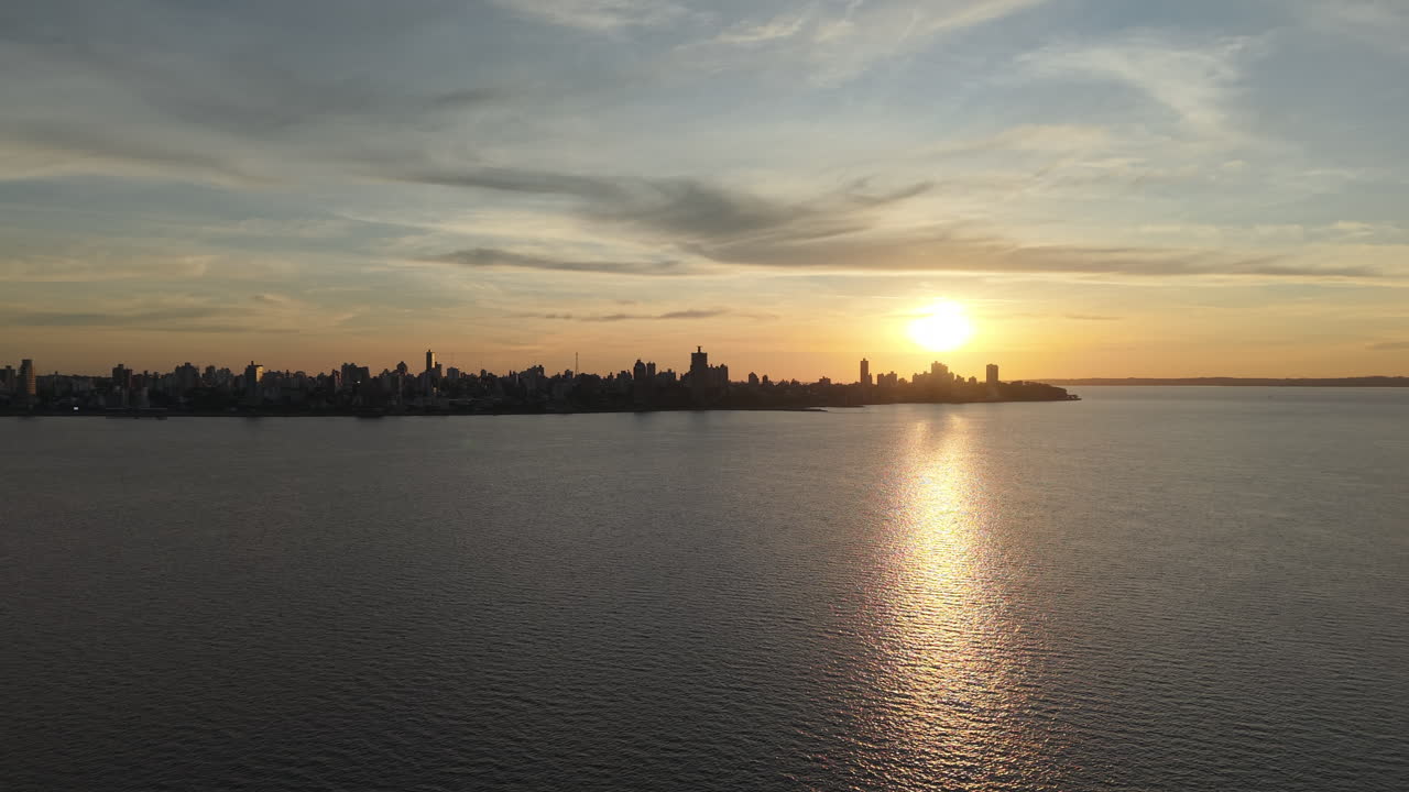 Sunset establishing over Posadas city skyline with calm river and glowing reflections