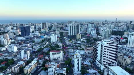 Urban-Caribbean-city-Santo-Domingo,-aerial-forward-at-blue-hour,-skyscrapers