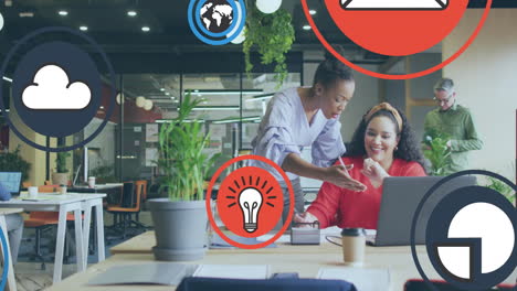 animation of icon in circles over diverse female coworkers discussing reports on laptop in office