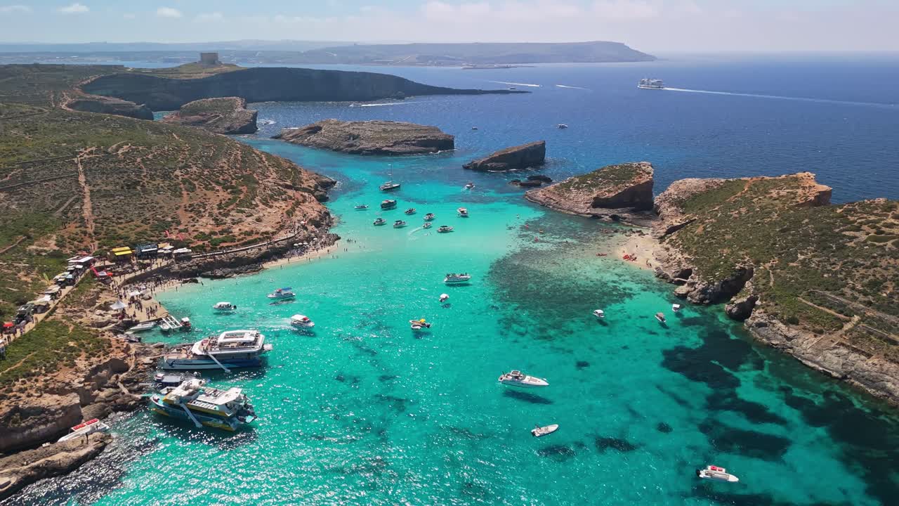 La Laguna Blu, Comino, Malta, presenta acque turchesi cristalline, coste rocciose e barche ancorate lungo la costa mediterranea in una pittoresca vista aerea in una soleggiata giornata primaverile.