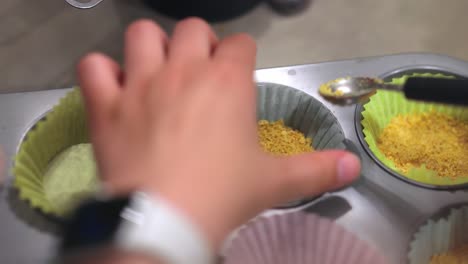 A-woman-pressing-down-cheesecake-crumb-base-into-a-cupcake-cup