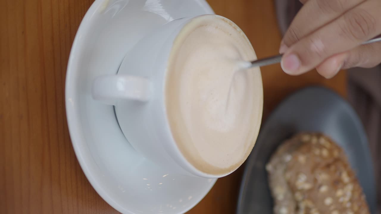 Hand Stirring Latte Coffee in White Cup on Wooden Table