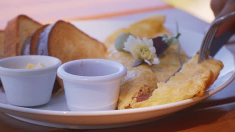 cutting and eating an omelette with bread and sauces in the morning for breakfast