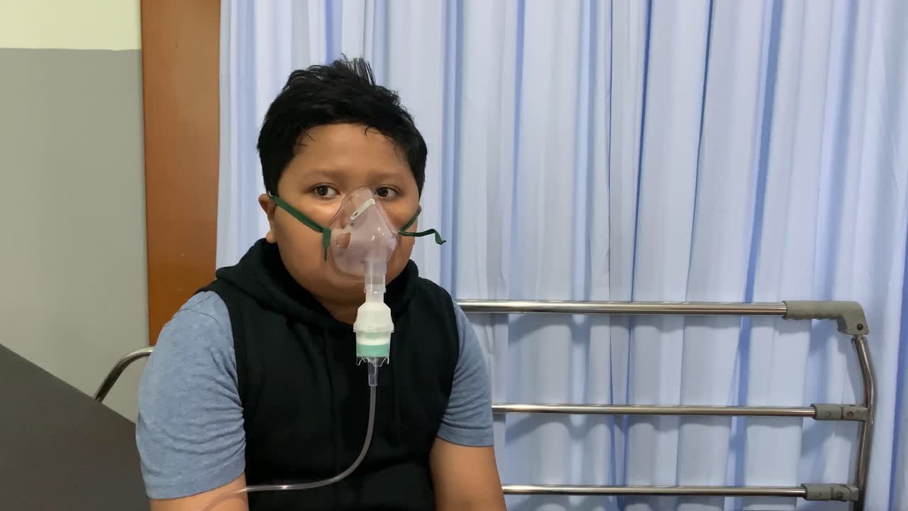 chico asiático hace inhalación con nebulizador en la cama del hospital