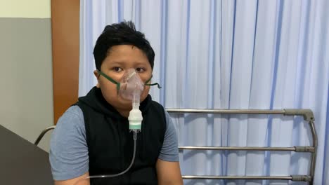 asian boy makes inhalation with nebulizer on hospital bed