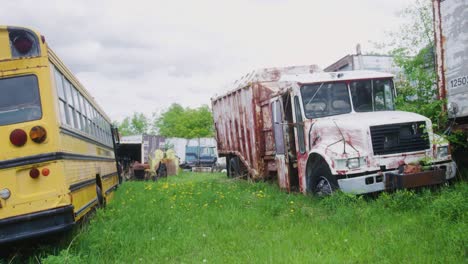 wide shot of an old school bus and a garbage truck sitting in the grass exposed to the elements