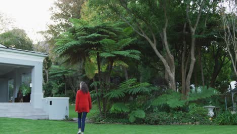 Rear-view-of-senior-caucasian-woman-walking-through-garden-towards-terrace