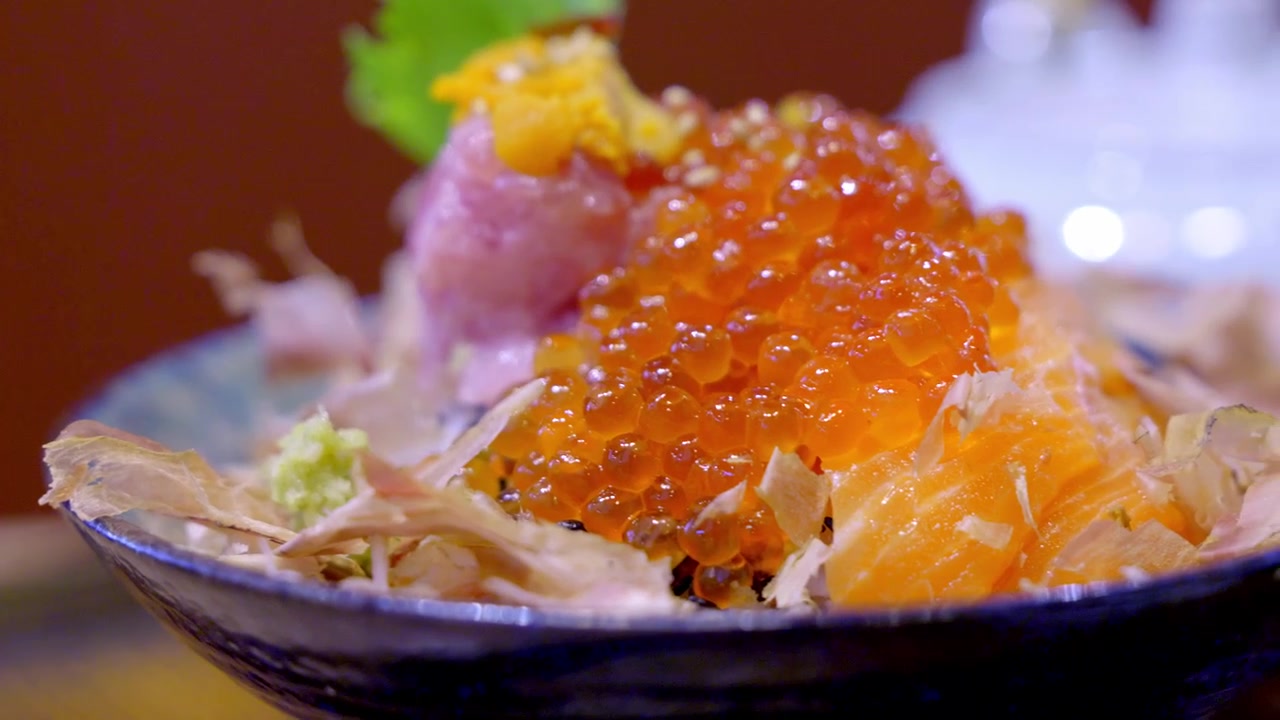 Close-up de uma tigela de donburi premium coberta com sashimi variado, uni cremoso e ovas de salmão vibrantes sobre arroz de sushi cozido no vapor, lindamente arranjado para uma elegante refeição japonesa.