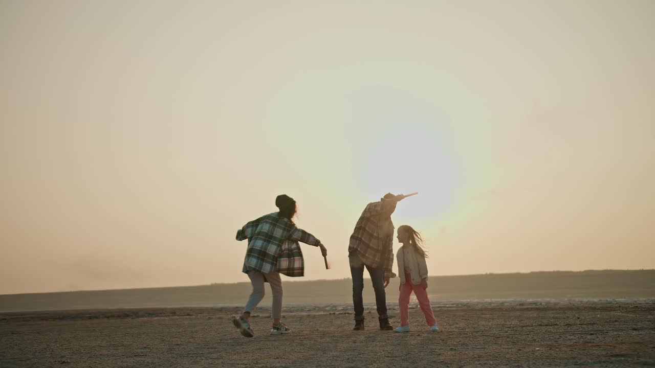 행복한 가족 중년 남자는 아내와 작은 딸과 함께 녹색과 빨간색 연기를 방출하는 불꽃놀이를 즐기며 여름 저녁에 도시 밖의 비어있는 사막 해변에서 애완 동물 크림색 개와 함께 휴식을 취합니다.