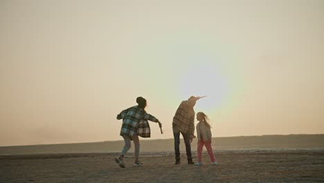 happy family middle-aged man with his wife and little daughter playing with fireworks that emit green and red smoke while relaxing with a pet cream-colored dog outside the city on an empty deserted seashore in the summer evening