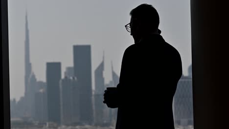 4k: silhouette of a businessman talking over the phone by the window, the world's tallest building 'burj khalifa' in the background