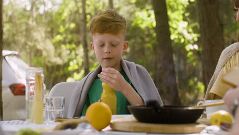 niño pequeño desayunando con su familia en el campamento en el bosque